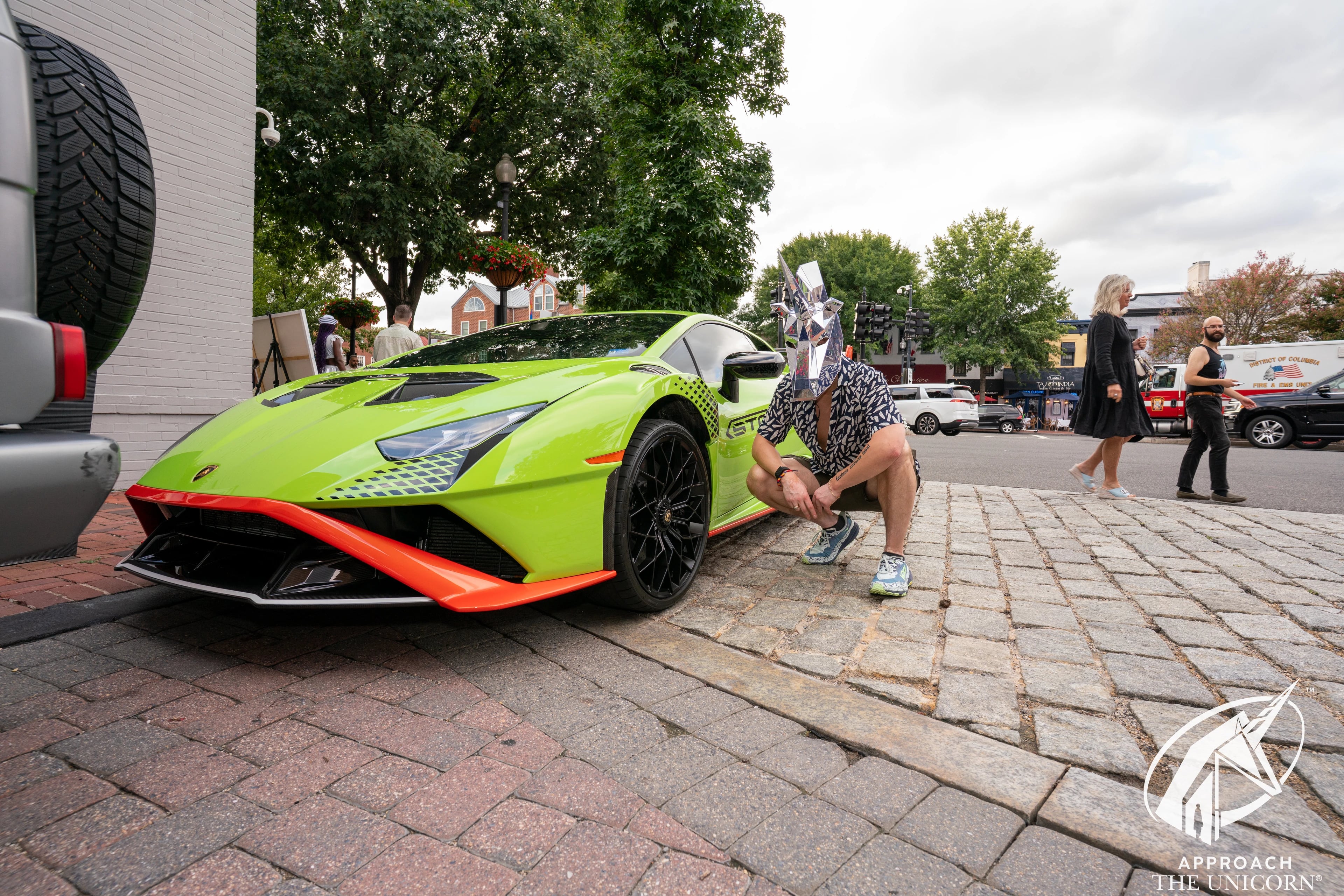 Guest wearing a mirrored unicorn head, kneeling beside a green Lamborghini at The Yacht Club